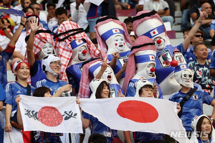 カッフィーヤ(アラブ伝統頭巾)風の赤白鉢巻にJAPANエンブレム、ピン隊が日の丸を掲げて応援（2022カタールW杯・日本vsドイツ／カリファ・スタジアム）